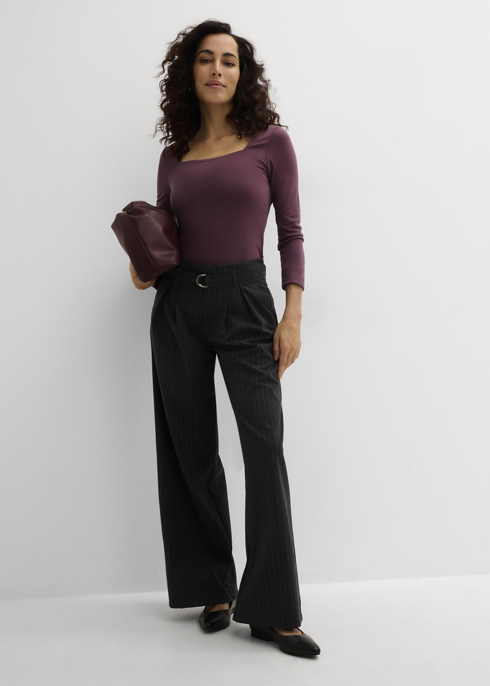 Lila Oberteil, gestreifte weite Hose, schwarze Schuhe und eine passende Handtasche.