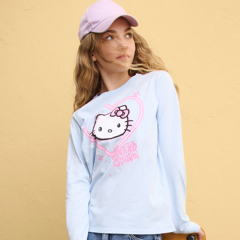 Blaues Langarmshirt mit Hello Kitty Aufdruck, blaue Jeans und rosa Cap.
