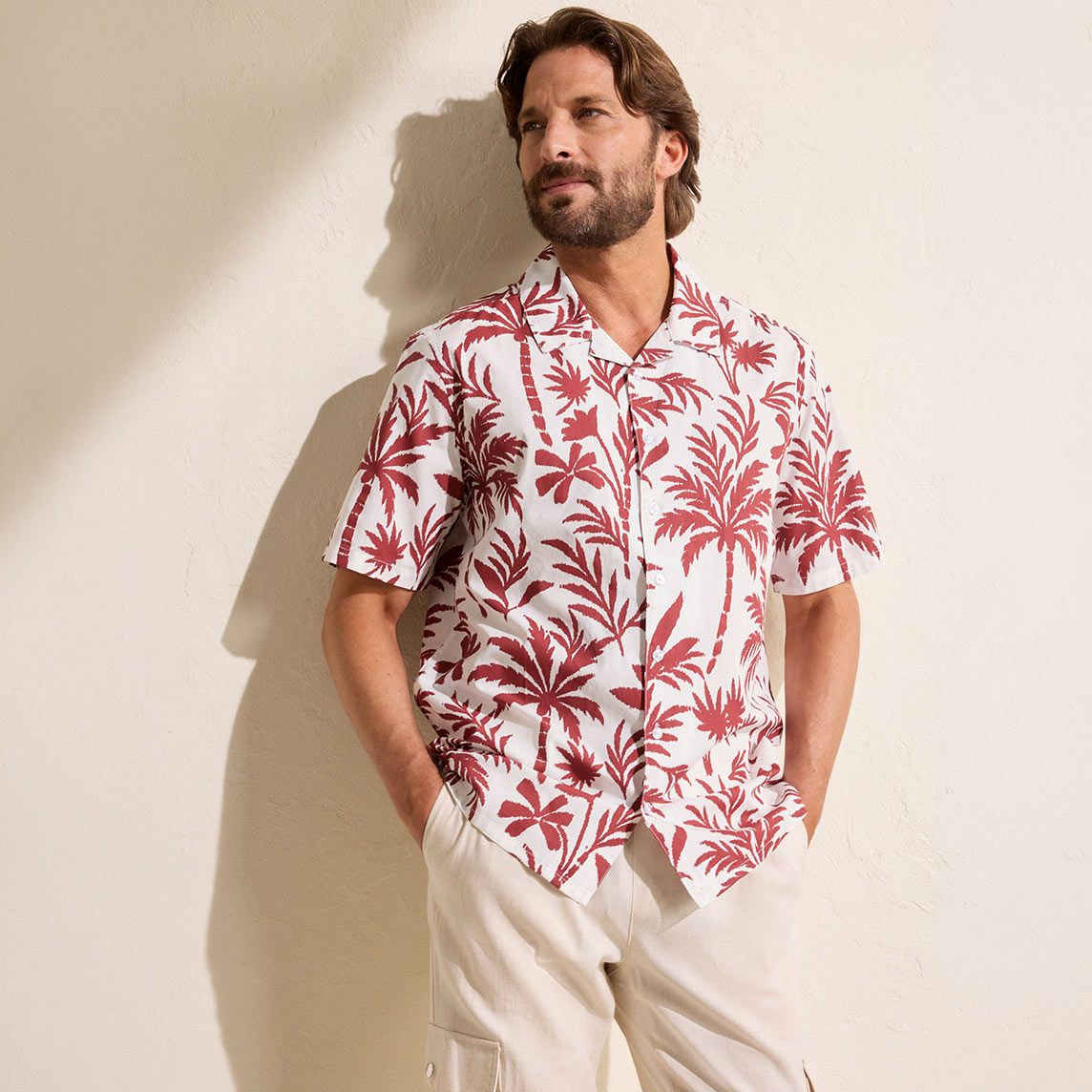 Mann trägt ein weißes Hawaiihemd mit roten Palmenmotiven und beige Hose.