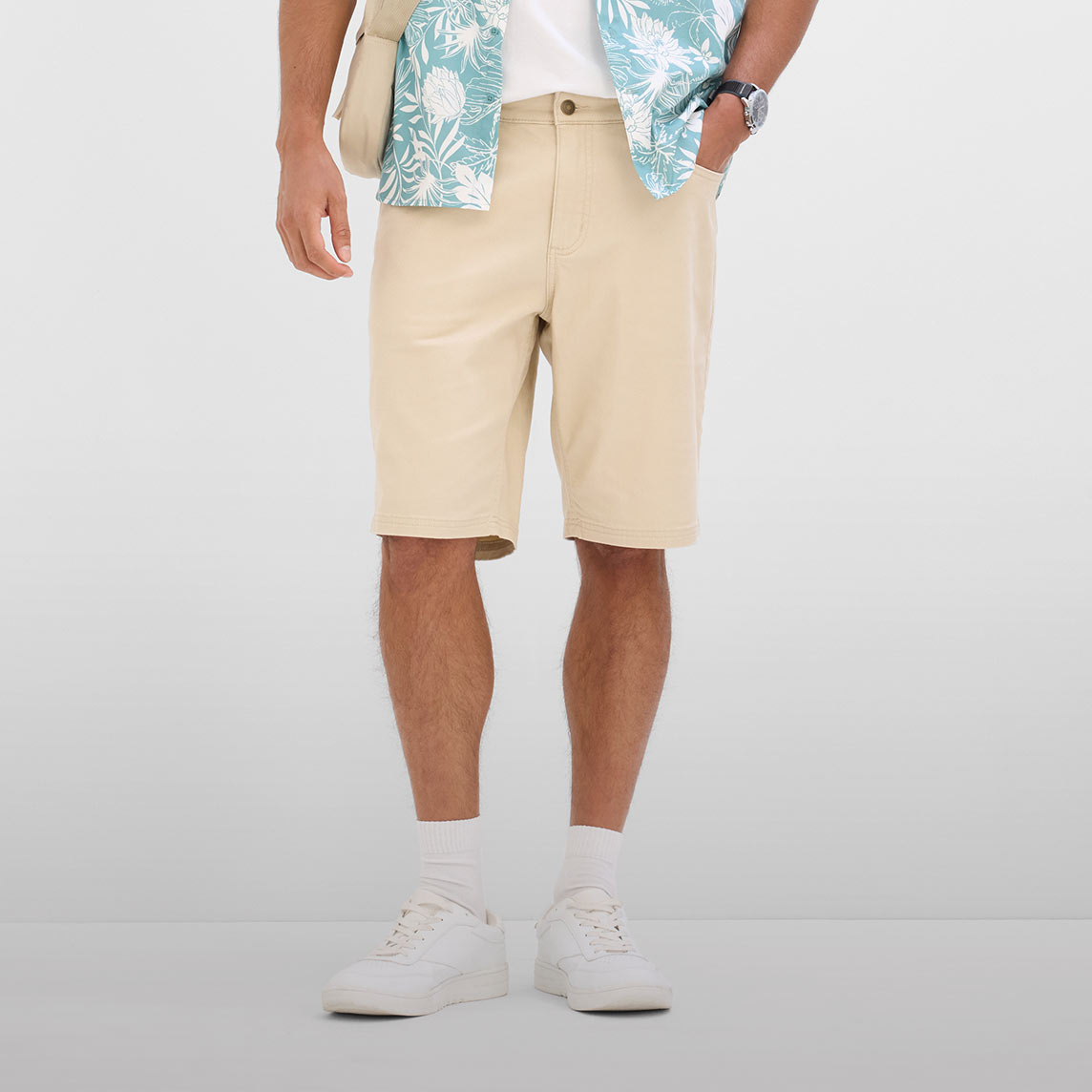 Lässiges Sommeroutfit mit beiger Bermuda-Shorts, gemustertem Hemd und weißen Sneakers.