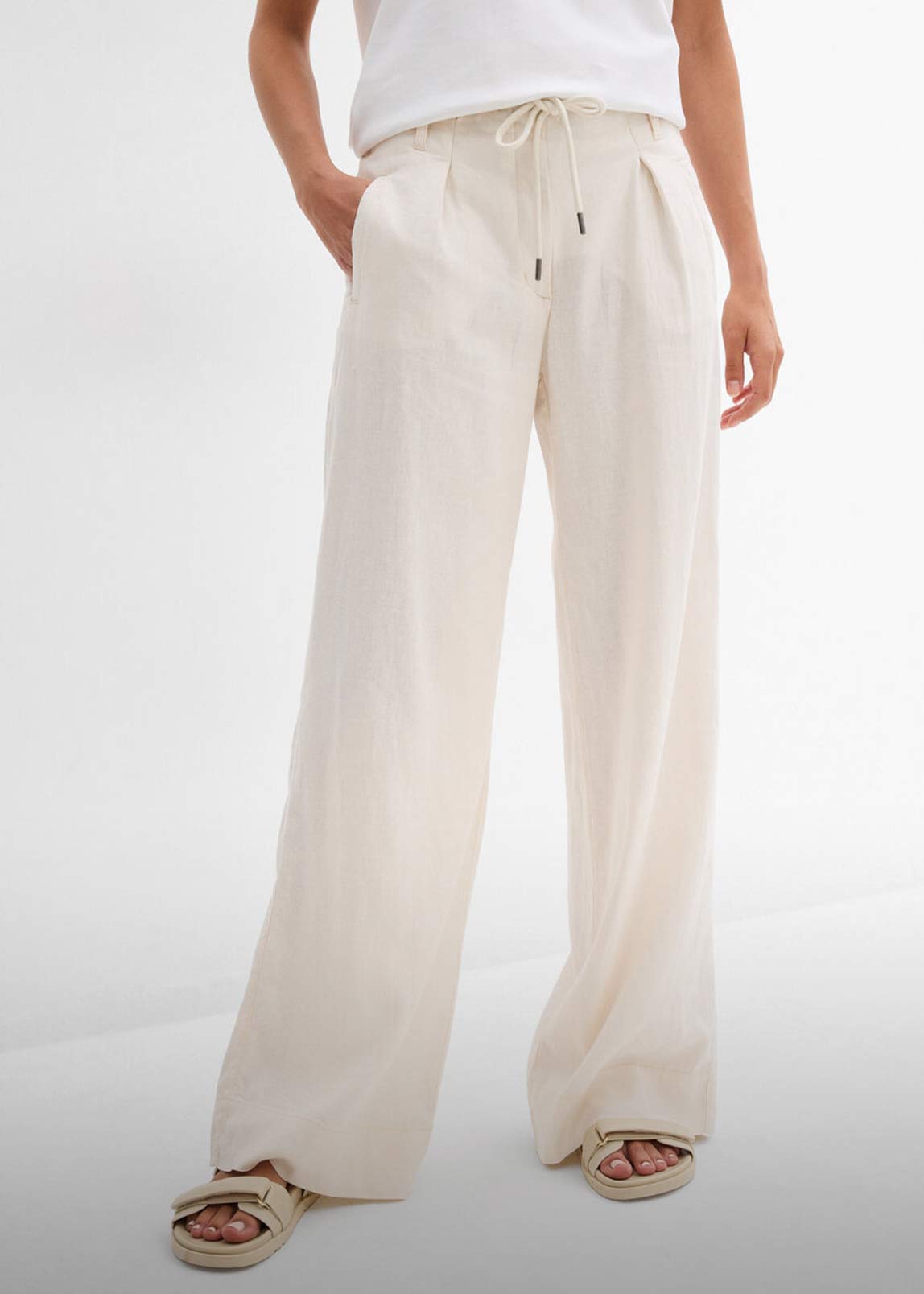 Weiße Leinenhose kombiniert mit schlichtem weißem Top und bequemen Sandalen.