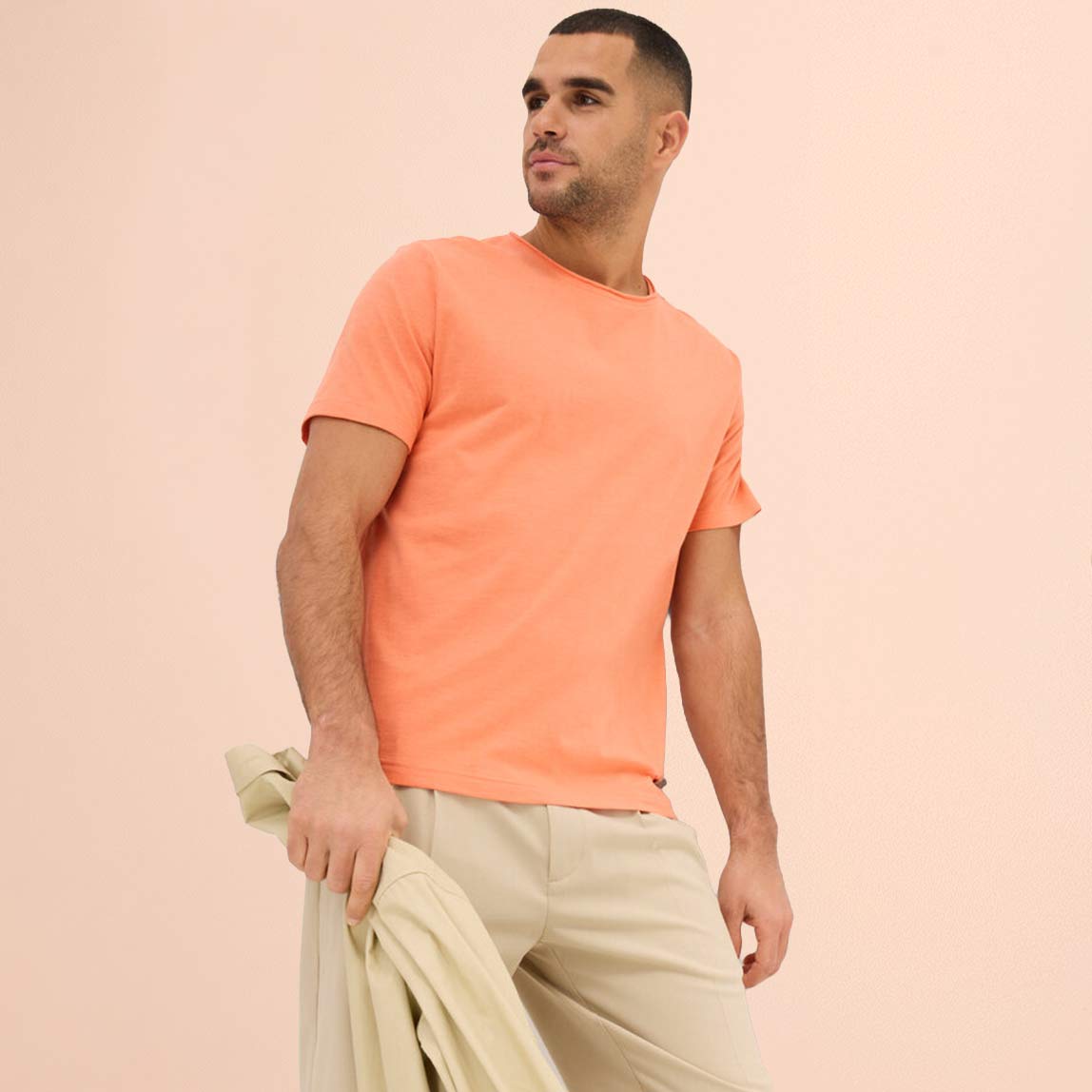 Pfirsichfarbenes T-Shirt kombiniert mit heller Hose und passendem Pullover als Accessoire.