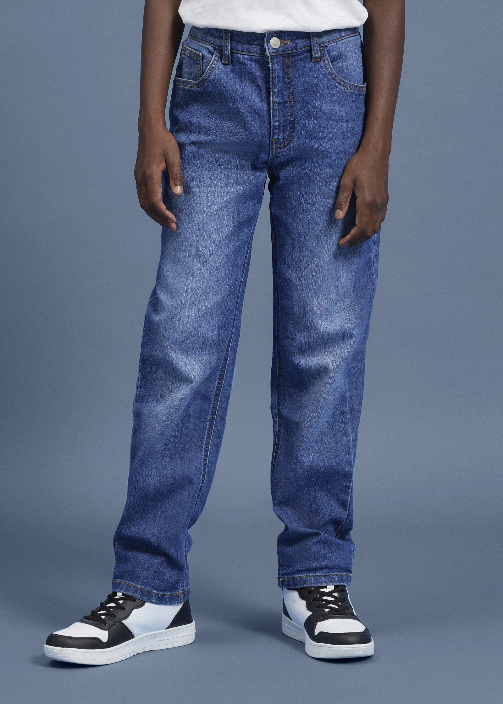 Blaue Jeans, ein weißes T-Shirt und schwarz-weiße Sneaker bilden das Outfit.