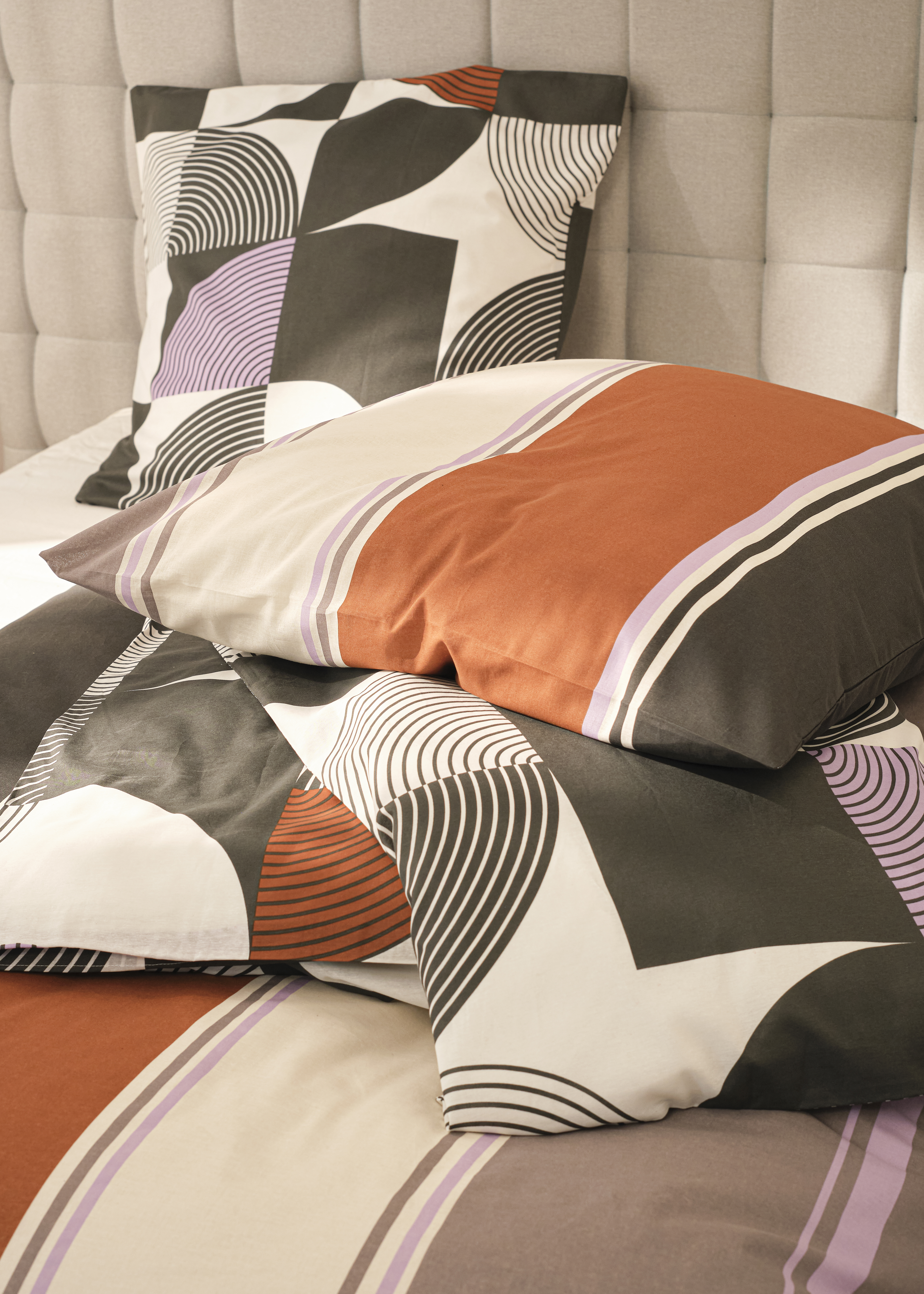 Geometrische Stoffmuster in Grau, Orange, Weiß und Lila.