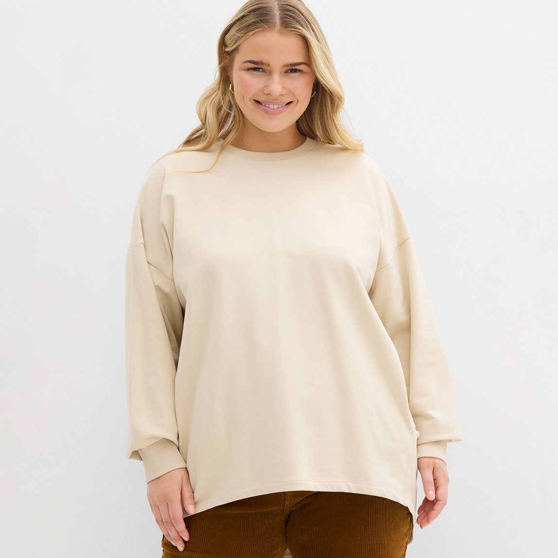 Cremefarbenes Sweatshirt mit Rundhalsausschnitt, kombiniert mit brauner Hose.