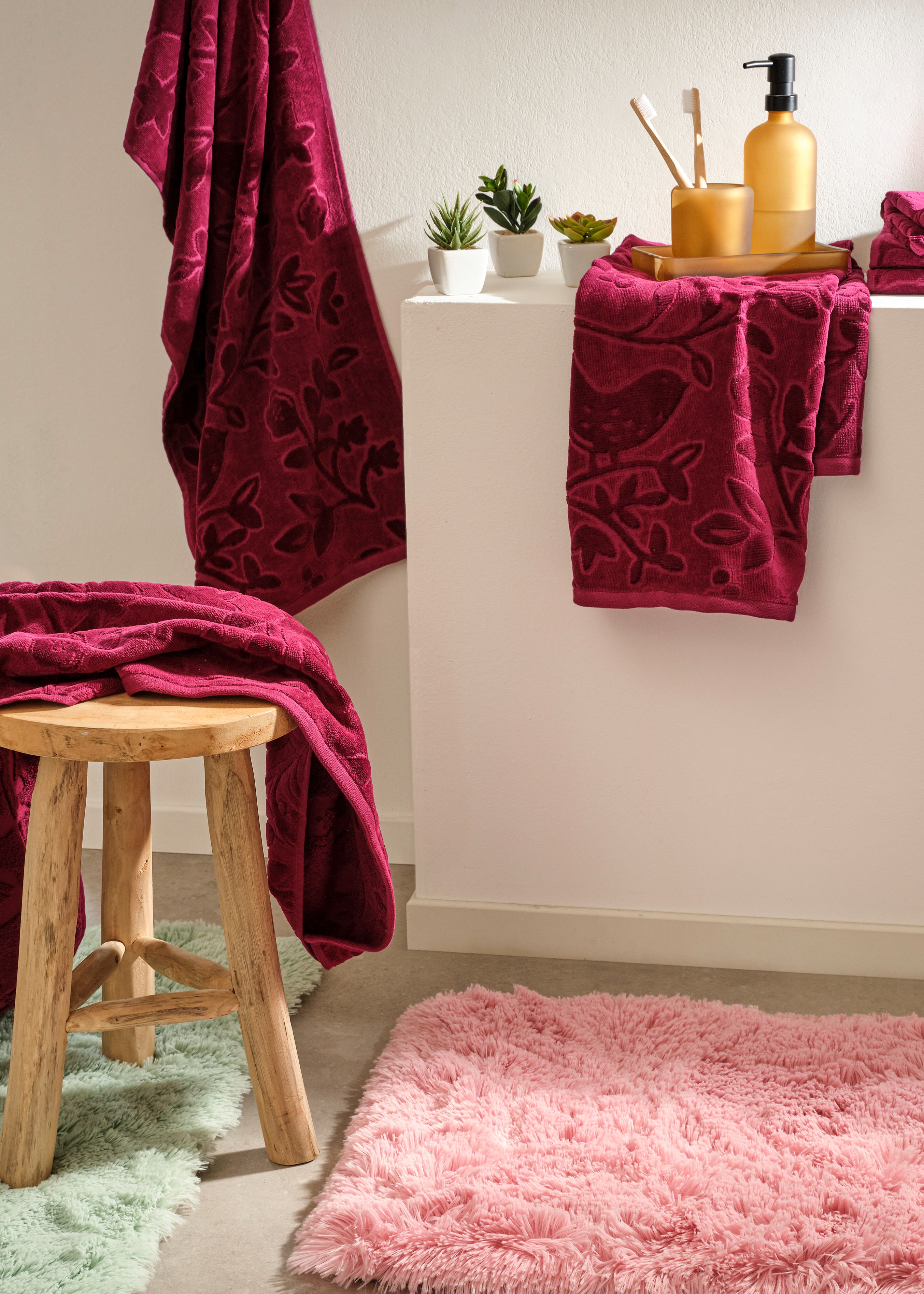 Flauschige Textilien in Bordeaux und Pastellrosa kleiden das Bad gemütlich ein.