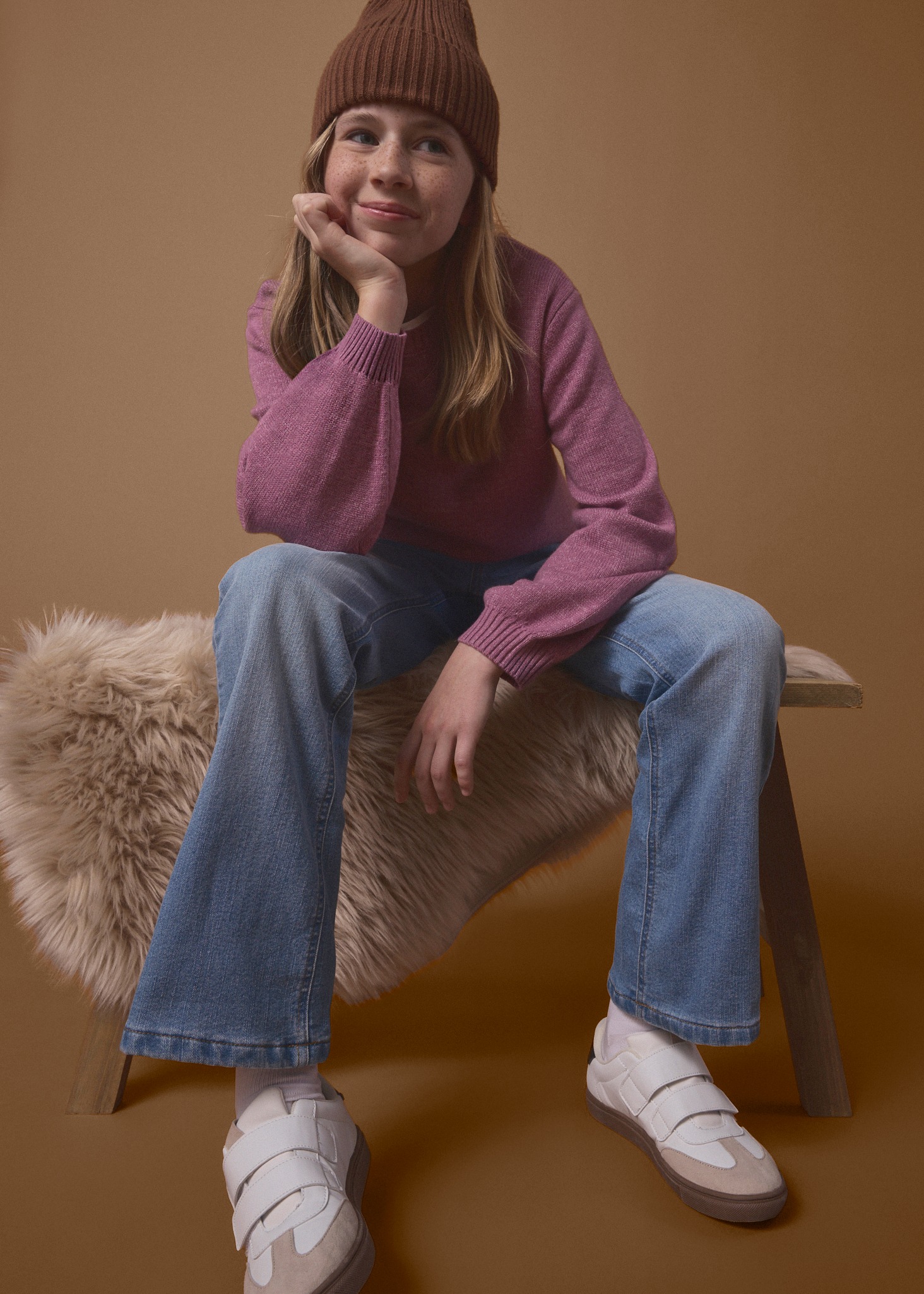 Braune Mütze, rosa Pullover, blaue Jeans und weiße Klett-Sneaker.
