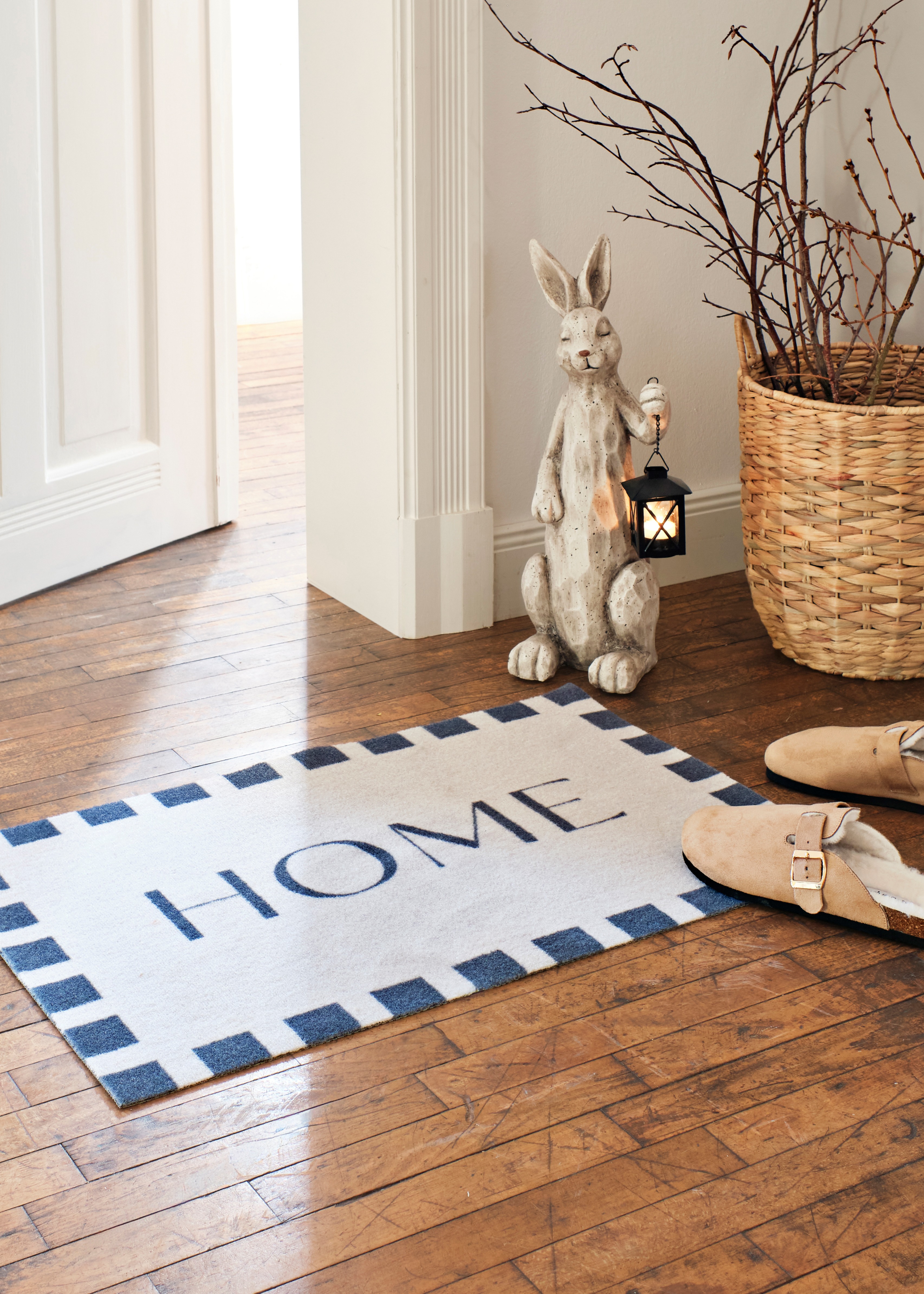 Fußmatte mit "HOME"-Schriftzug, neben einer dekorativen Hasenfigur.