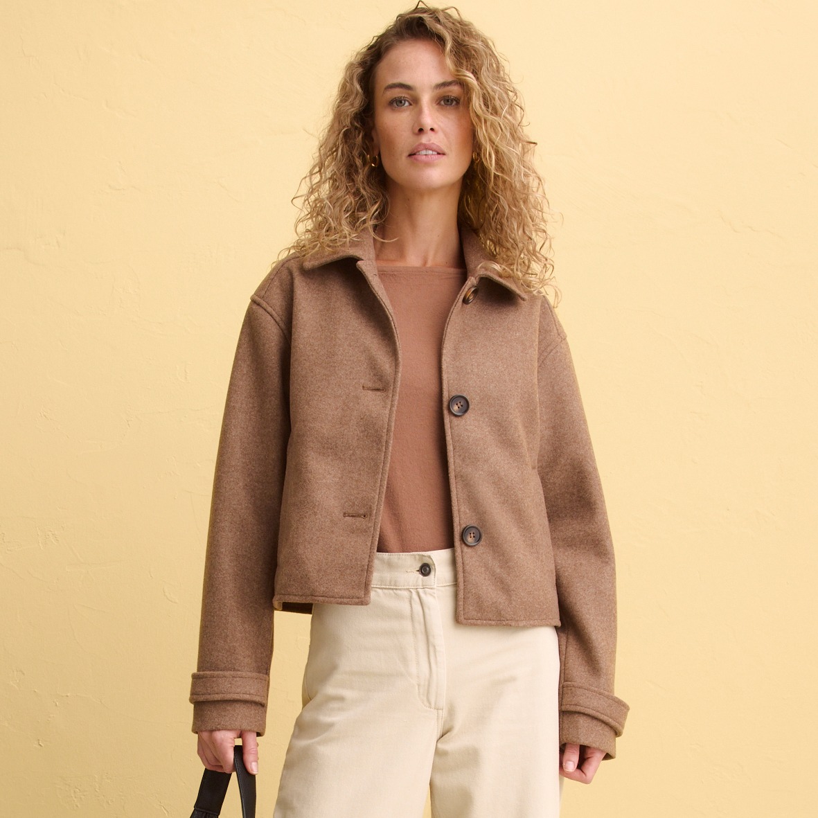 Elegante braune Kurzjacke über zartem Top, kombiniert mit heller Hose.