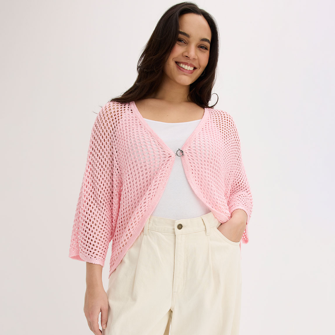 Frau trägt rosafarbene Strickjacke über weißem Top und cremefarbener Hose.