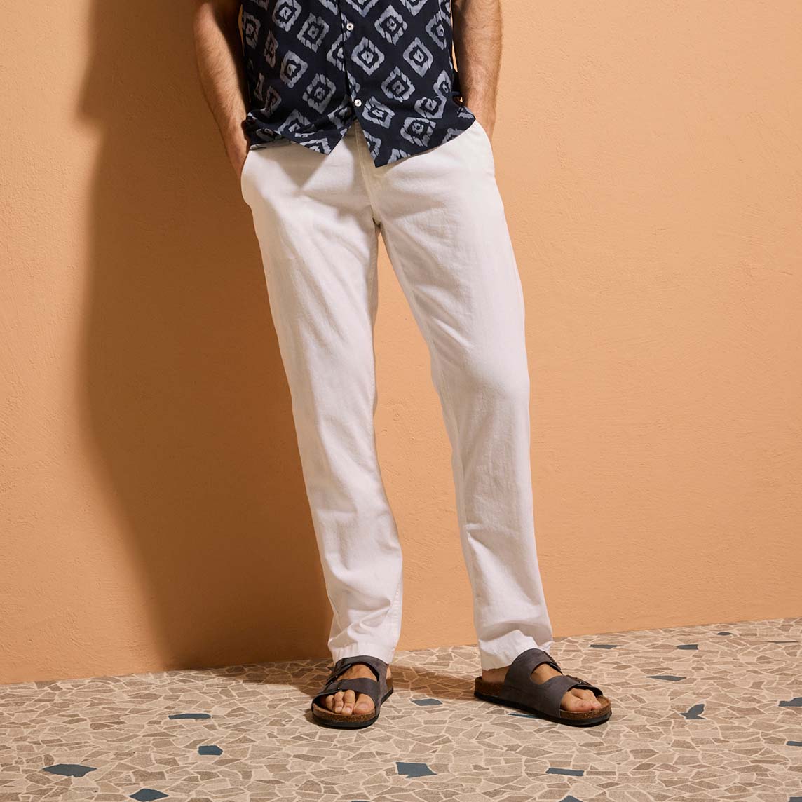 Weiße Stoff-Hose, gemustertes dunkles Oberteil und schwarzen Sandalen.