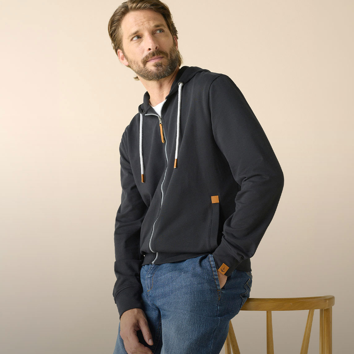 Dunkler Reißverschluss-Sweatjacke, hellblaue Jeans, weißes Shirt.