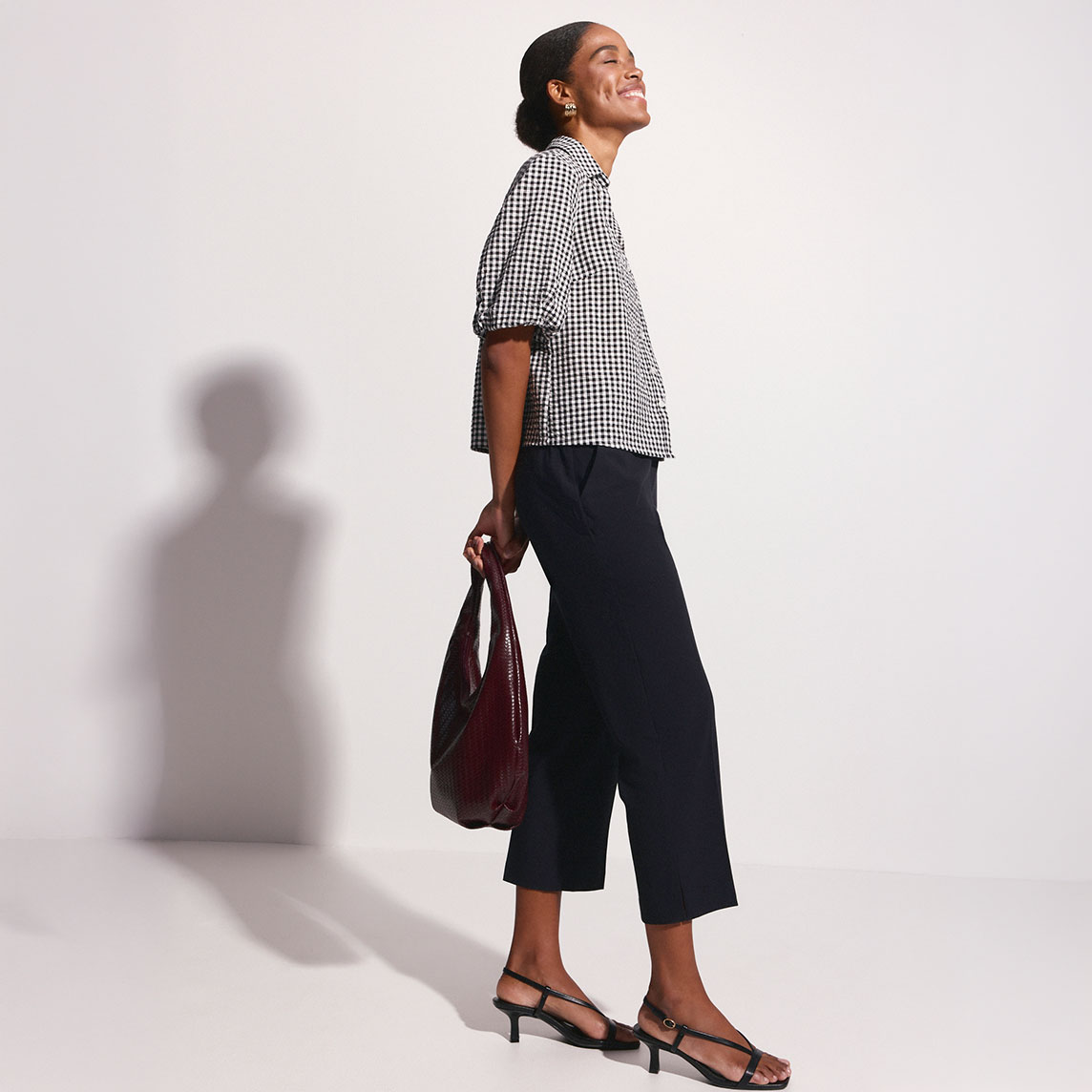 Stilvolle Kombination: Karierte Bluse, dunkle Culotte-Hose und elegante Riemchensandalen mit Tasche.