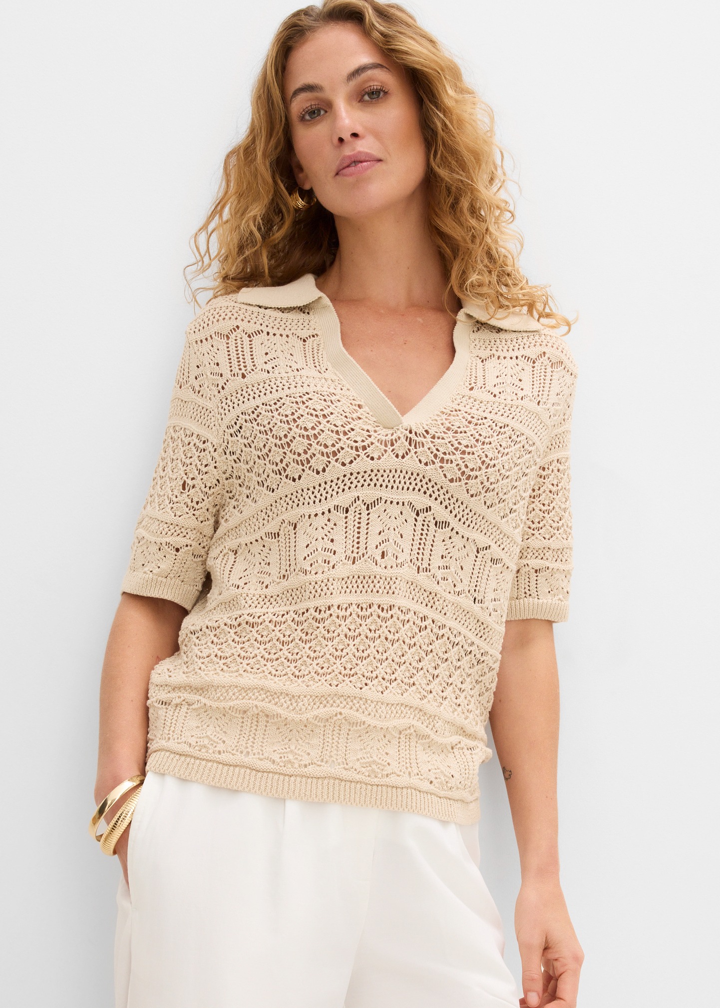 Beiger Ajour-Polo-Pullover mit V-Ausschnitt und filigranem Lochmuster, dazu weiße Hose.