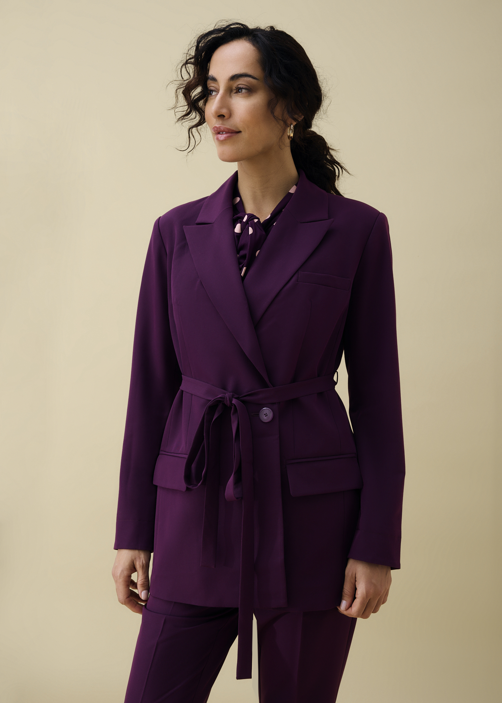 Eleganter violetter Blazer mit Gürtel und passender Hose, dazu eine gepunktete Bluse.