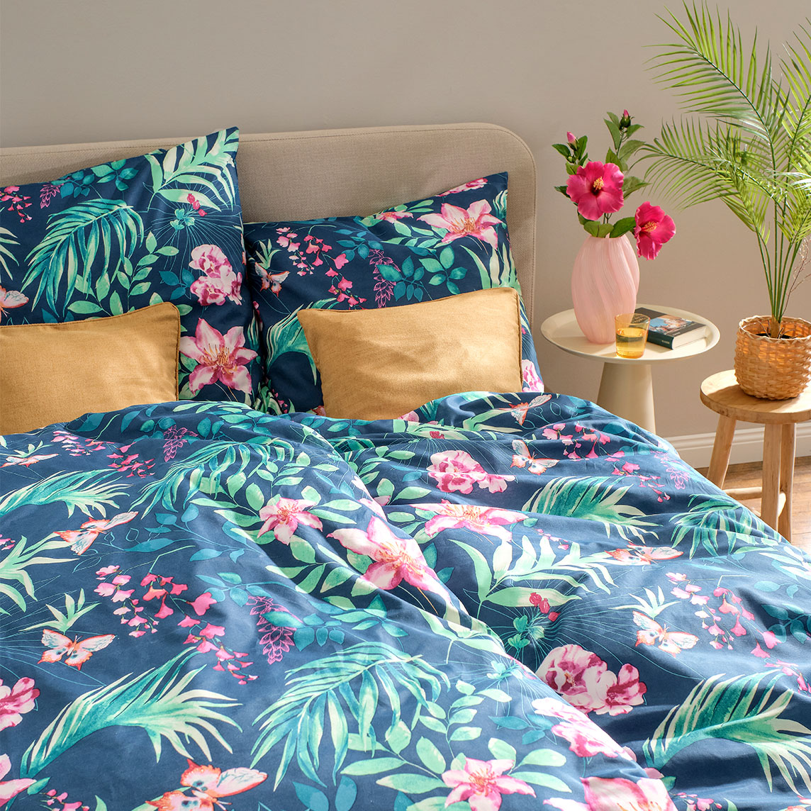 Bunte Bettwäsche mit tropischem Blumenmuster in Blau- und Grüntönen schmückt das gemütliche Schlafzimmer.