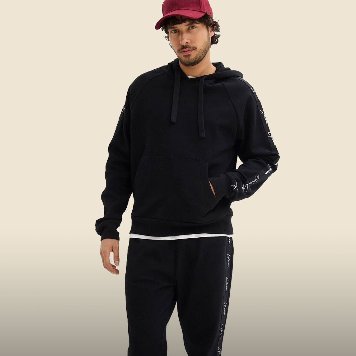 Lässiger schwarzer Hoodie und Jogginghose mit Schriftzügen, dazu rote Kappe.