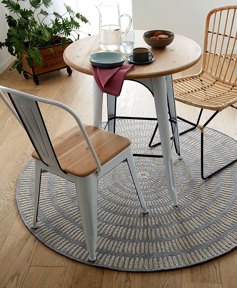 Eine gemütliche Essecke mit rundem Teppich, metallenen Stühlen und einem hölzernen Tisch.