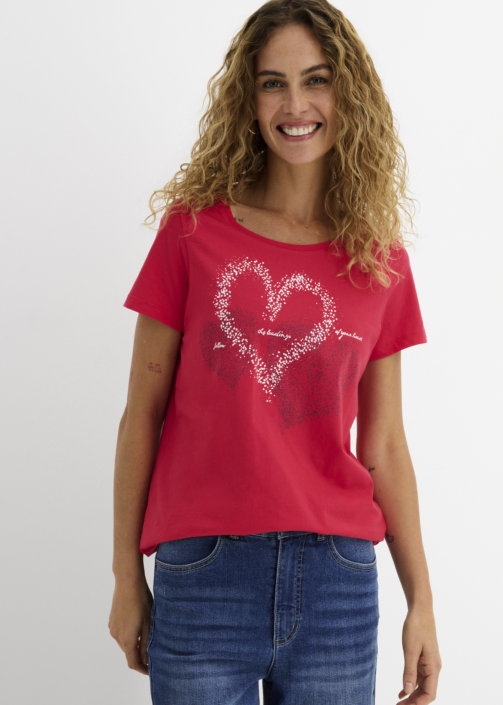 Stilvolles rotes T-Shirt mit glitzerndem Herzmotiv, kombiniert mit blauen Jeans.