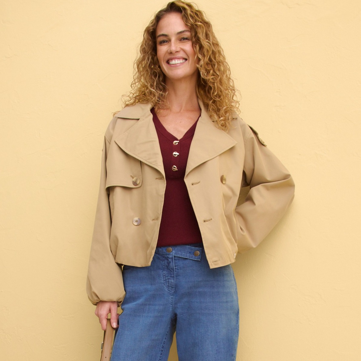 Beige Jacke über weinrotem Top, kombiniert mit blauen Jeans.