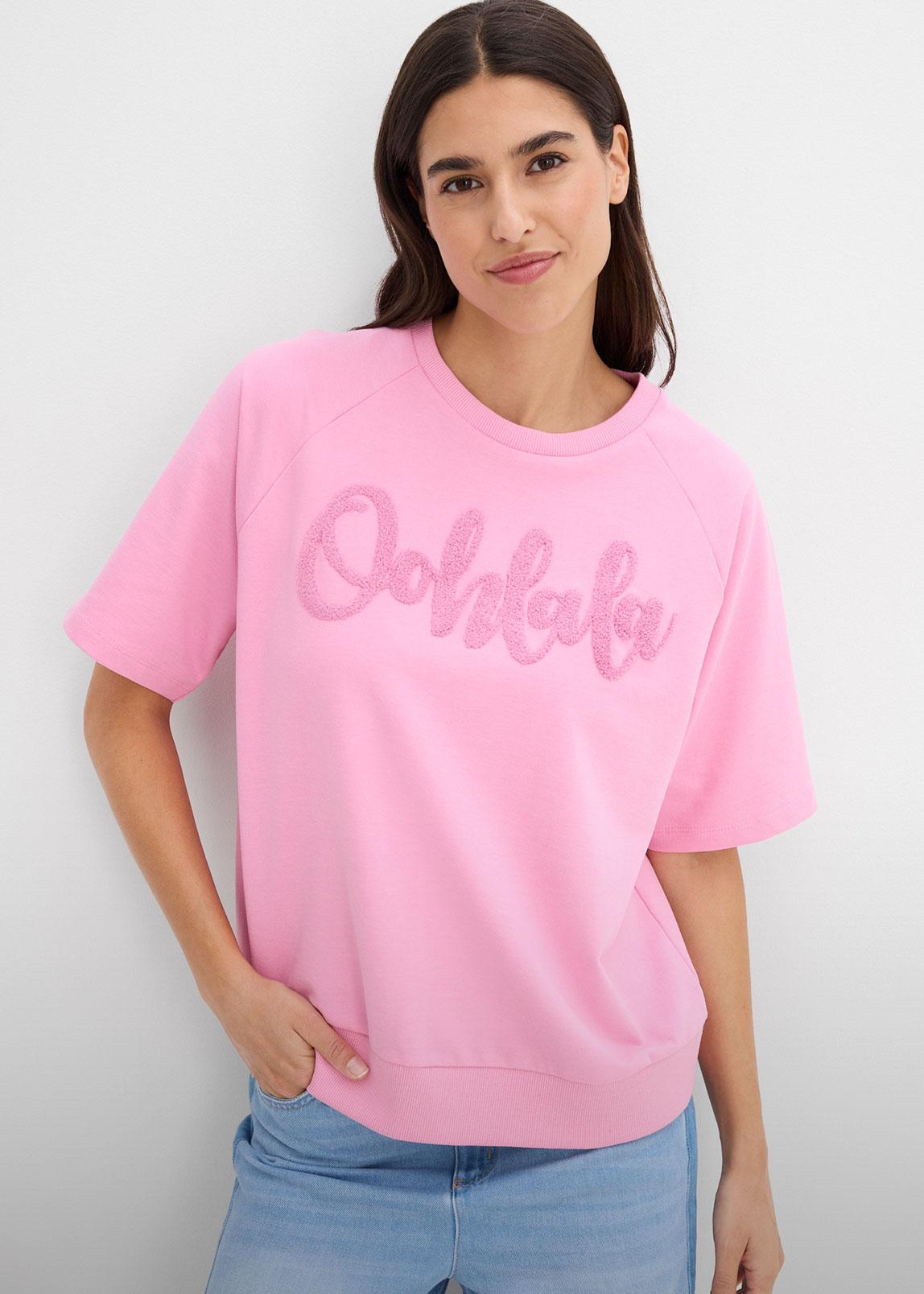 Lässiges rosa Kurzarm-Sweatshirt mit auffälliger "Oohlala"-Stickerei, kombiniert mit heller Jeans.