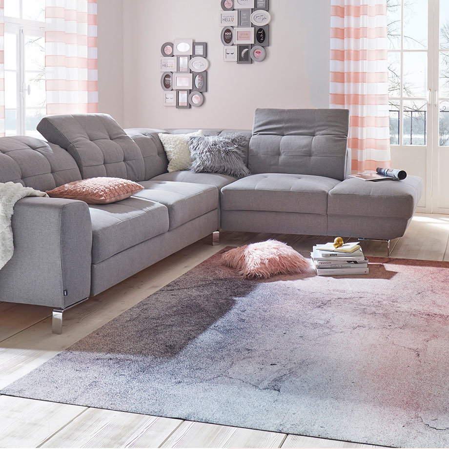 Gemütliches graues Ecksofa mit Kissen, umgeben von weichen Teppichen und dezenter Wanddekoration.