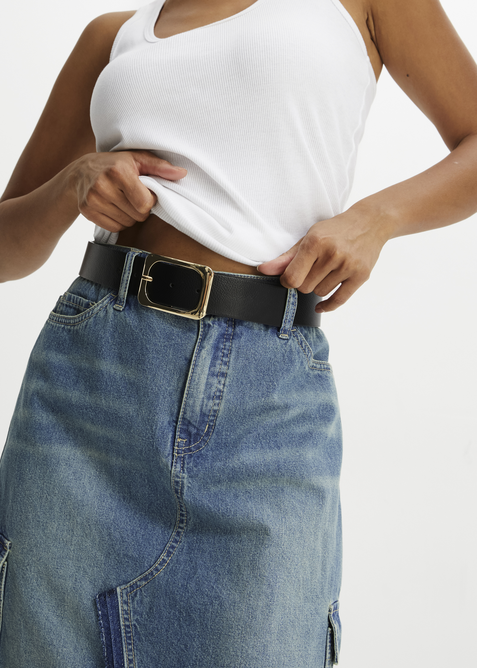 Lässiger Sommerlook: Weißes Tanktop, helle Jeans-Shorts und breiter Ledergürtel mit goldener Schnalle.