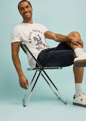 Mann trägt weißes T-Shirt mit Print und dunkle Shorts in entspannter Pose.