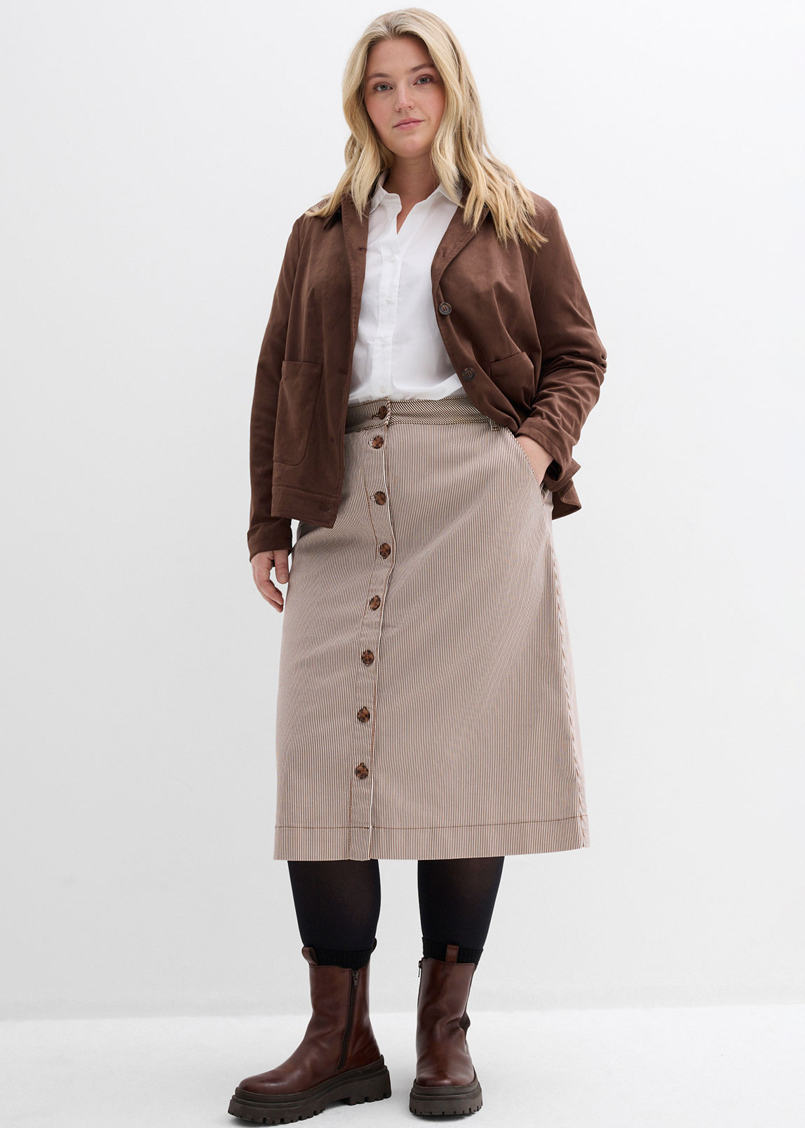Braune Jacke, weiße Bluse, gestreifter Knopfrock und braune Boots.