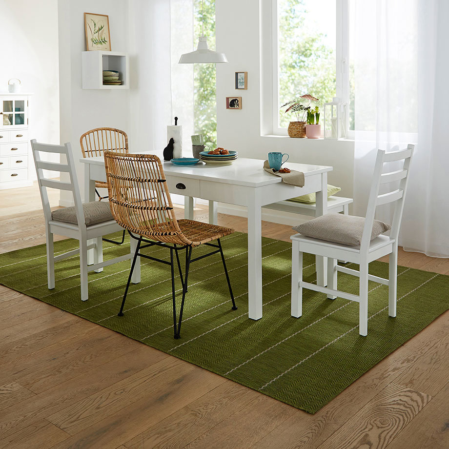 Ein weißer Esstisch mit weißen Holzstühlen und einem goldenen Drahtkorb-Stuhl auf grünem Teppich.