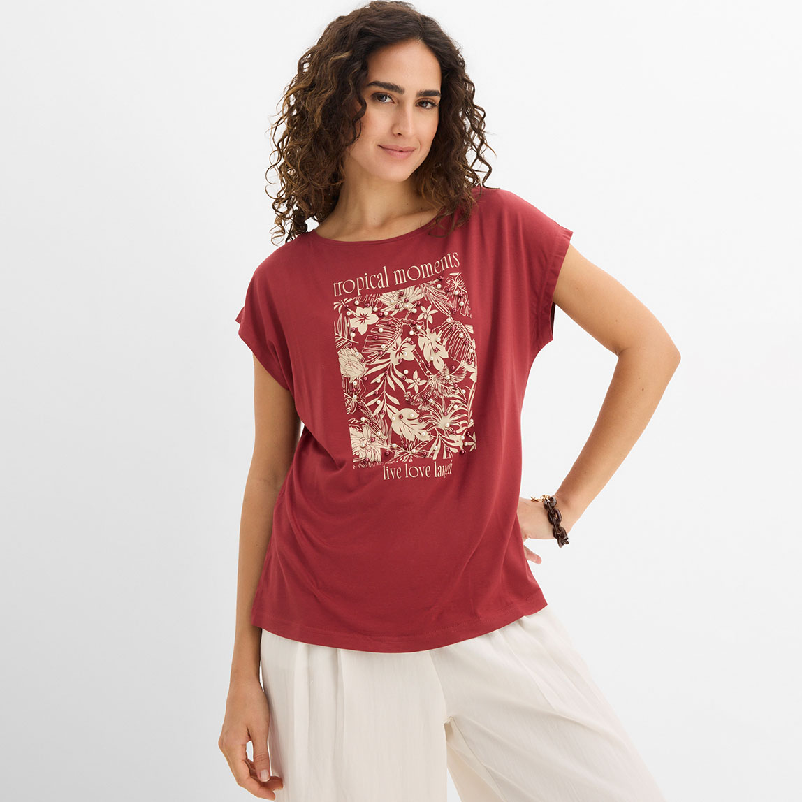 Frau trägt rotes T-Shirt mit weißem Aufdruck und beige Hose in lässigem Stil.