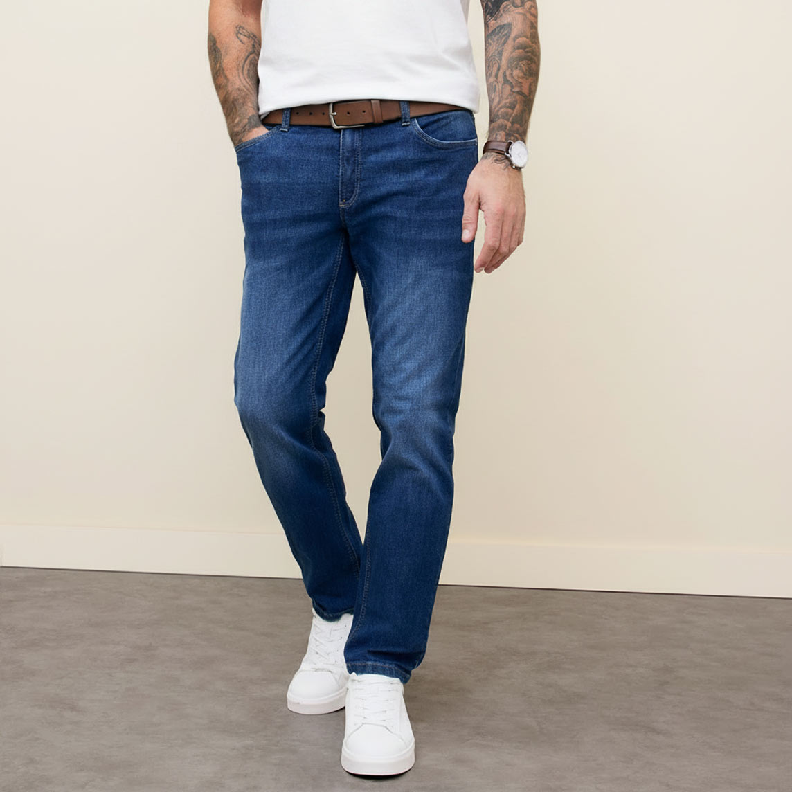 Klassischer Look mit weißem T-Shirt, blauer Jeans, braunem Ledergürtel und weißen Sneakern.