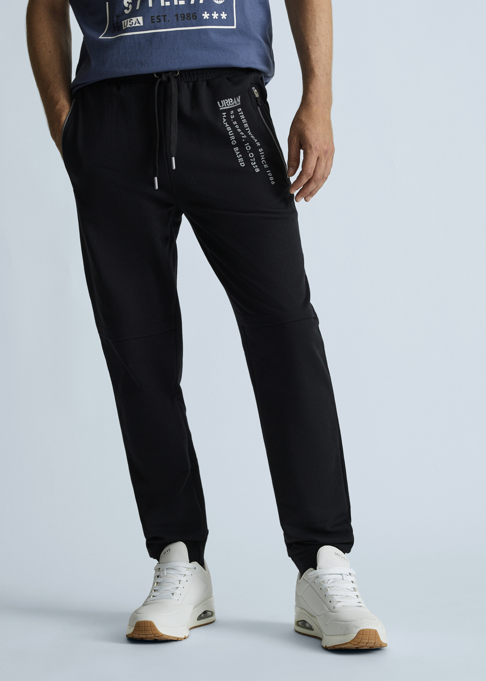 Schwarze Jogginghose, bequemes T-Shirt und weiße Sneaker für einen sportlichen Look.